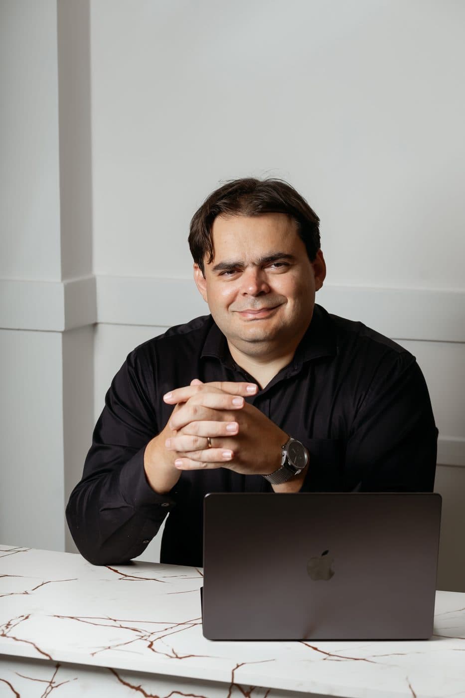 Murilo Martins sentado à mesa, com um notebook, sorrindo