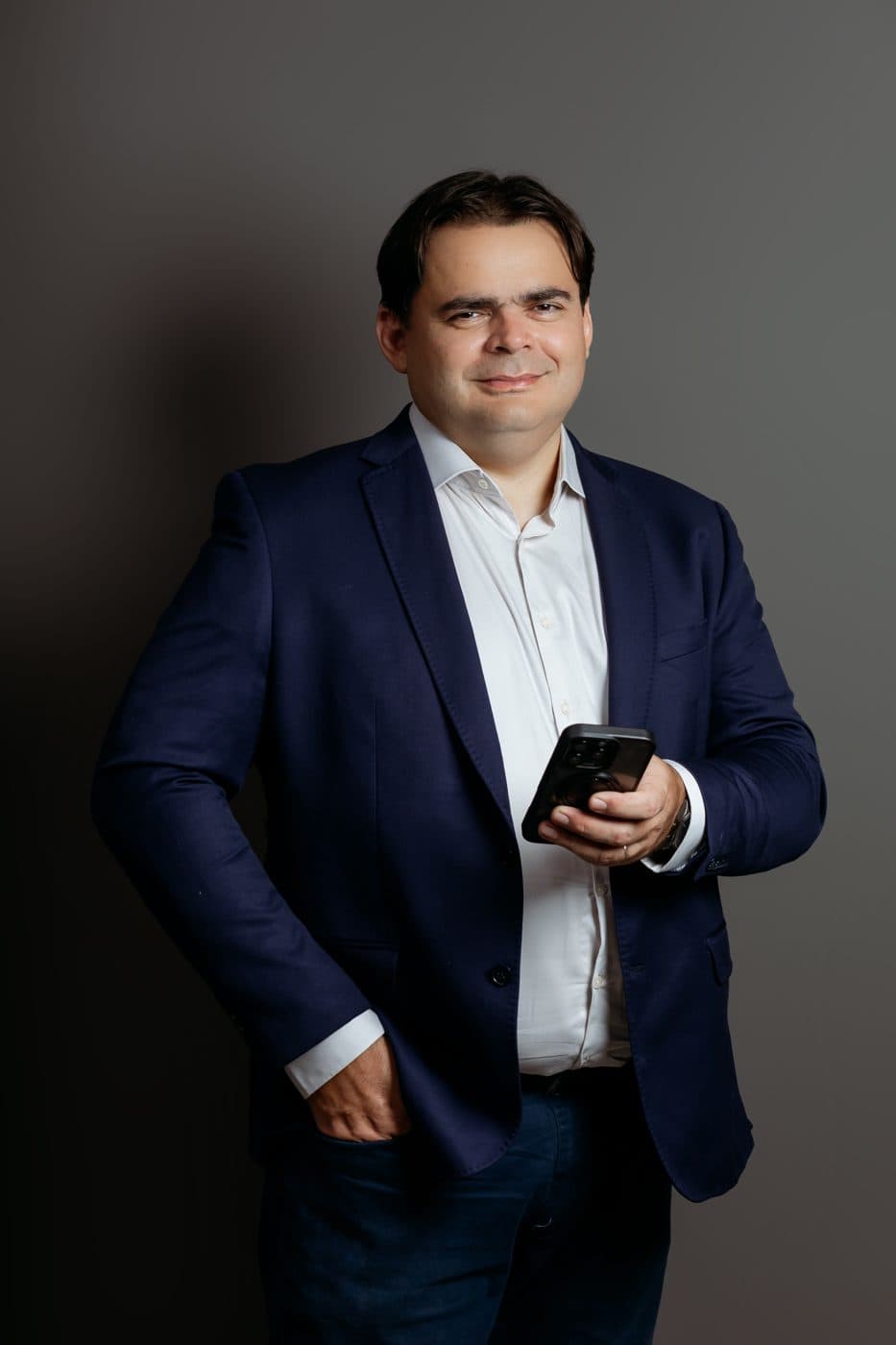 Murilo Martins, de blazer azul, sorrindo com o celular na mão
